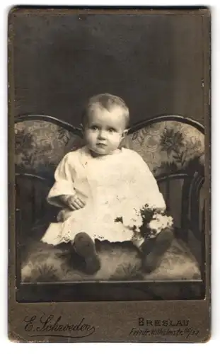 Fotografie E. Schroeder, Breslau, Friedr. Wilhelmstr. 60 /62, Kleines Mädchen mit Blumen auf einem gepolsterten Stuhl