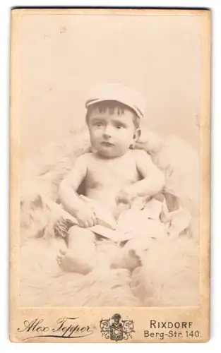 Fotografie Alex Tepper, Rixdorf, Berg-Str. 140, Kleines Baby mit einer Schiebermütze auf einem Pelz