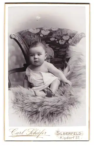 Fotografie Carl Schäfer, Elberfeld, Kipdorf 57, Neugieriges Baby in weissem Leinen auf einem Pelz