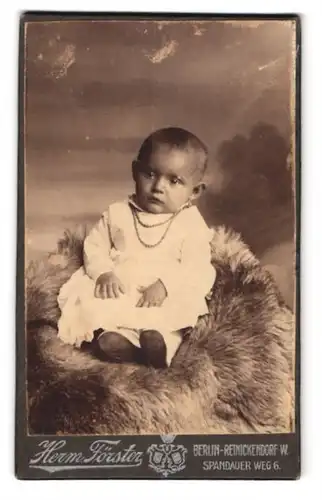 Fotografie Herm. Förster, Berlin-Reinickendorf, Spandauer Weg 6, Süsses Kleinkind im Kleid sitzt auf einem Fell