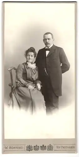 Fotografie W. Höffert, Berlin, Mann und Frau im Anzug mit Fliege und im Kleid sitzend im Stuhl