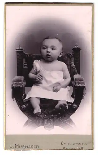 Fotografie J. Mürnseer, Karlsruhe, Rüppurrer-Str. 16, Erstauntes Kleinkind in weissem Kleid auf Stuhl