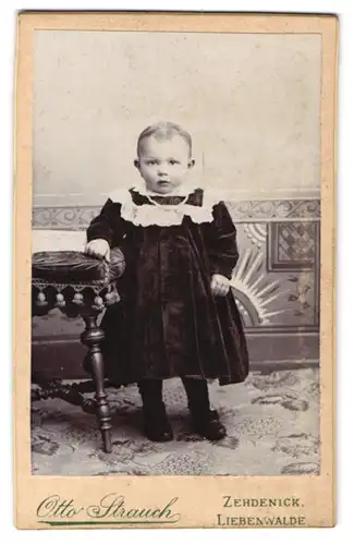 Fotografie Otto Strauch, Zehdenick, Berlinerstr. 22, Ernstes Kleinkind in dunklem Kleid mit Rüschen