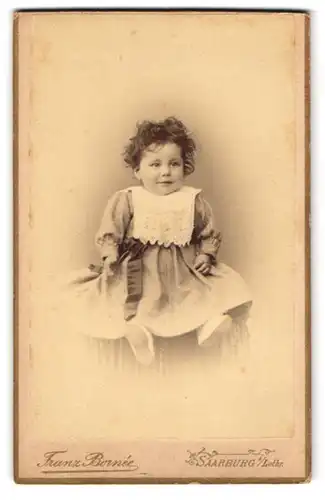 Fotografie Franz Bornée, Saarburg /Lothr., Lupinstr. 53, Kleines Mädchen im schicken Kleid mit Schleife an der Hüfte