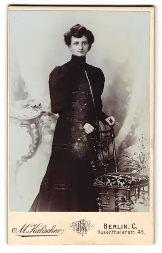 Fotografie M. Kalischer, Berlin C., Rosenthalerstr. 45, Junge Dame in schwarzem Kleid mit Puffärmeln an einem Stuhl