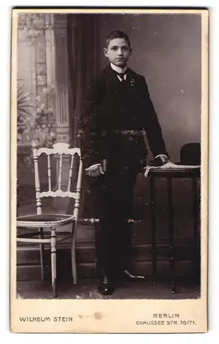 Fotografie Wilhelm Stein, Berlin, Chaussee Str. 70 /71, Knabe im Anzug mit Krawatte, seine Lederhandschuhe in der Hand
