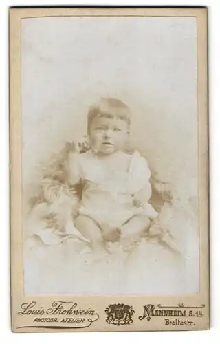 Fotografie Louis Frohwein, Mannheim, Breiterstr., Kleinkind in weissem Kleid mit vollem Haar auf einem Pelz