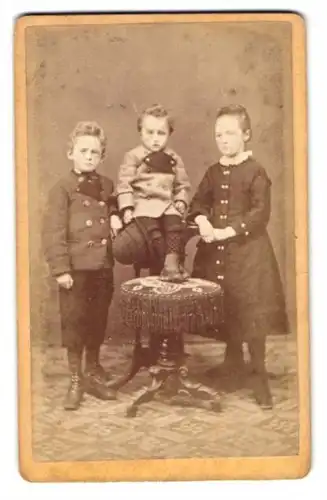 Fotografie F. Steigenberger, Weilheim, Drei Kinder in ihrer Sonntagsgarderobe, das jüngste auf einer Empore sitzend