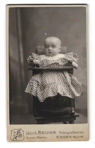 Fotografie Louis Becker, Essen /Ruhr, Einhornstrasse 3, Baby im schicken gepunkteten Kleid im Babystuhl