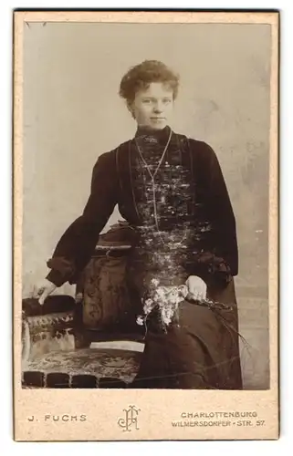 Fotografie J. Fuchs, Charlottenburg, Wilmersdorfer Str. 57, Junge Dame im eleganten Kleid mit weiten Ärmeln, mit Blume