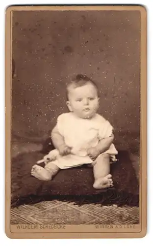 Fotografie Wilhelm Schlöbcke, Winsen a. d. Luhe, Süsses Kleinkind im Hemd sitzt auf Kissen