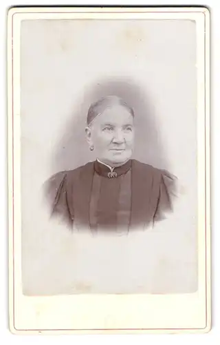 Fotografie Oscar Milan, Görlitz, Alte Dame mit adrett zurückgestecktem Haar im schwarzen Kleid mit Brosche am Kragen