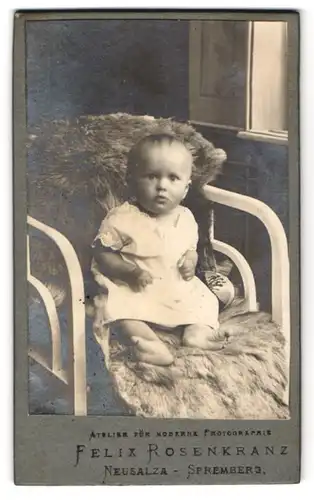 Fotografie Felix Rosenkranz, Neusalza-Spremberg, Kleinkind mit erwartungsvollem Blick und geballten Fäusten auf dem Pelz