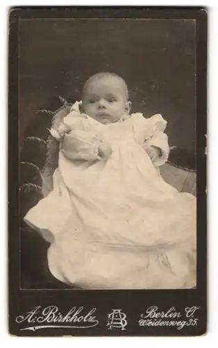Fotografie A. Birkholz, Berlin O., Weidenweg 35, Kleines Baby mit erstauntem Blick und geballten Fäusten im weiten Kleid