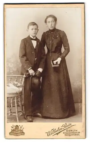 Fotografie Wilhelm Stein, Berlin, Chausseestr. 66, Mädchen im schwarzen Kleid mit verzierter Brustpartie nebst Bruder
