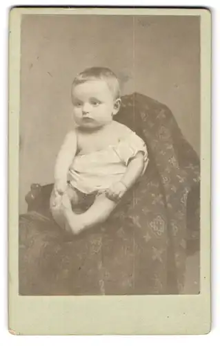Fotografie unbekannter Fotograf und Ort, Kleinkind im weissen Gewand auf einer gemusterten Decke