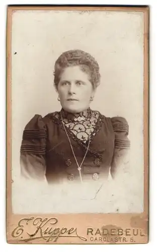 Fotografie E. Kuppe, Radebeul, Carolastr. 5, Elegante Dame in dunklem Kleid mit Lockenfrisur u. langer Kette