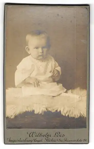 Fotografie Wilhelm Loos, Augustusburg i Erzgeb., Marienbergerstr. 25, Trotziges Kleinkind in weissem Kleid auf Fell