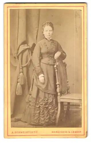 Fotografie A. Schweisfurth, Remscheid, Elegante Dame mit Flechtfrisur stehend in tailliertem Kleid