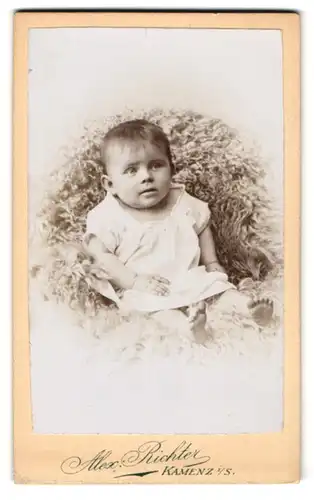 Fotografie Alex Richter, Kamenz i. S., Kleinkind in weissem Kleid sitzt auf einem Schafsfell