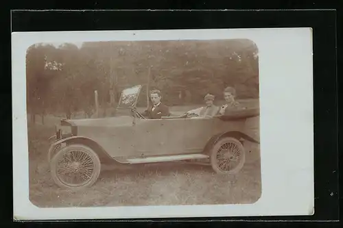 Foto-AK Auto, Junger Mann am Steuer, zwei Frauen auf der Rückbank, KFZ auf einer Wiese