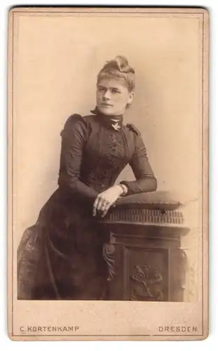 Fotografie C. Kortenkamp, Dresden, Annenstr., Junge Dame im schwarzen taillierten Kleid mit Zierelementen auf der Brust