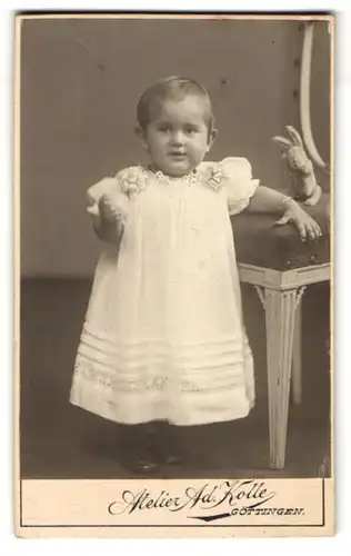 Fotografie Ad. Kolle, Göttingen, Printenstr. 18, Kleines Mädchen im langen weissen Kleid neben ihrem Spielzeughasen