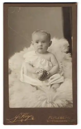 Fotografie J. Heyn, Perleberg, Wittenbergstr. 86, Blondes Kleinkind in weissem Kleid mit Ball auf Fell