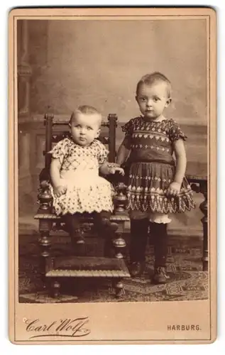 Fotografie Carl Wolf, Harburg, Junges Mädchen mit kurzem Haar und verziertem Kleid mit ihrer kleinen Schwester