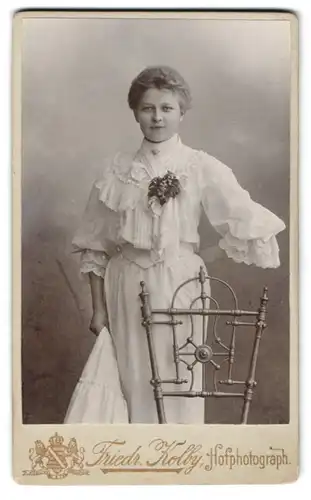 Fotografie Friedr. Kolby, Zwickau i. S., äuss. Plauensche Str., Junge Frau im weissen Rüschenkleid mit angesteckter Blume