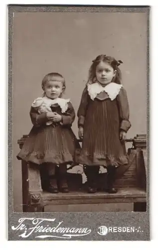 Fotografie Tr. Friedemann, Dresden, Rosenstr. 48, Niedliche junge Schwestern in dunklen Kleidern mit Puppe und Schleifen