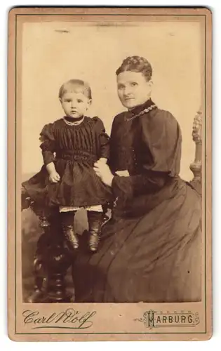 Fotografie Carl Wolf, Harburg, Gurbürgerliche Mutter mit niedlicher Tochter in schwarzen Kleidern am Tisch