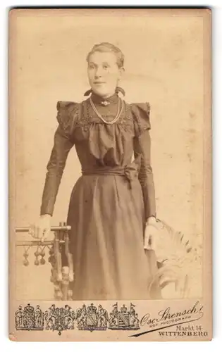 Fotografie Osc. Strensch, Wittenberg, Markt 14, Junge Frau im schwarzen Kleid mit Schleife und Brosche am Lächeln