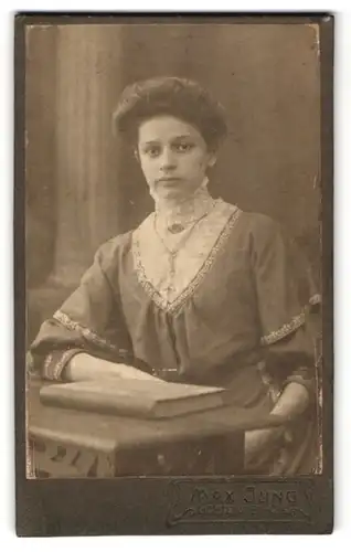 Fotografie Max Jung, Lichtenstein, Junge Frau im Kleid mit weisser Spitze und Brosche nebst Buch