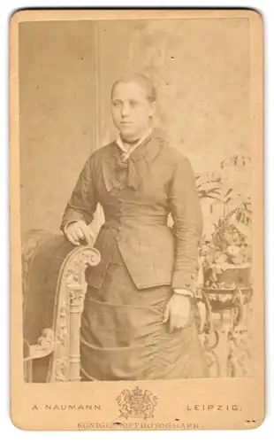 Fotografie A. Naumann, Leipzig, Dorotheenstr. 12, Junge Frau im taillierten Kleid mit Spitze und Brosche nebst Blumen