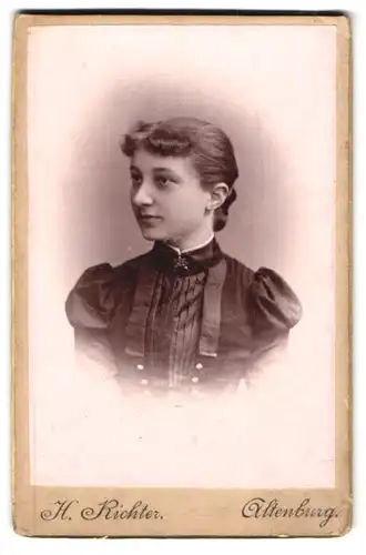Fotografie H. Richter, Altenburg, Hübsche junge Frau im schwarzen Kleid mit Brosche und hochgesteckten Haaren