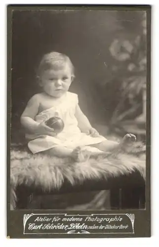 Fotografie Curt Schröder, Döbeln, Niedliches Baby im weissen Kleid mit missmutigem Blick und Ball in der Hand