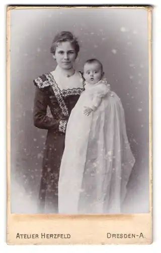 Fotografie Atelier Herzfeld, Dresden, Junge schöne Mutter im schwarzen Kleid mit Baby im weissen Kleid auf dem Arm