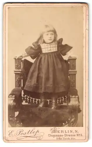 Fotografie E. Postlep, Berlin, Chaussee-Str.5, Niedliches kleines Mädchen im schwarzen breiten Kleid auf Stuhl stehend