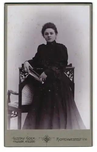 Fotografie Gustav Gock, Hohenwestedt, Schöne junge Frau im schwarzen Kleid mit Zeitung gelehnt an einen Stuhl