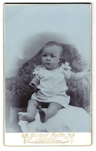 Fotografie Reinhard Radtke, Liebenwerda, Süsse Baby im weissen Kleid mit Schleifen und Keks in der Hand