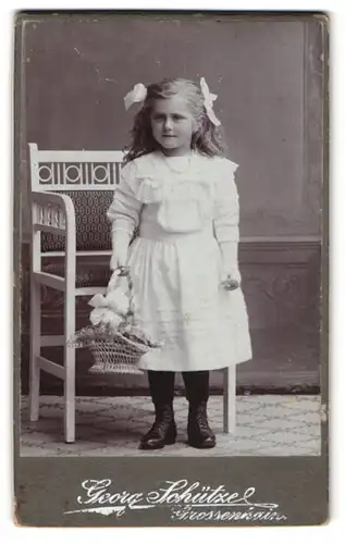 Fotografie Georg Schützel, Grossenhain, Junges Mädchen im weissen Kleid mit zwei Schleifen im Haar und einem Korb Blumen