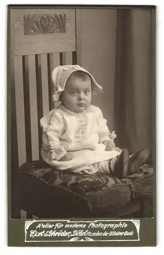 Fotografie C. Schröder, Döbeln, Kleinkind im weissen Kleid mit Musterung auf Brust und Ärmeln und einer Kappe