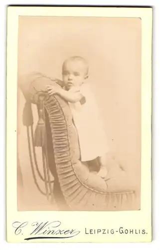 Fotografie C. Winzer, Leipzig-Gohlis, Äussere Halleschestr. 50, Süsses Kleinkind im Kleid steht auf Sessel