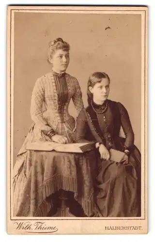 Fotografie Wilh. Thieme, Halberstadt, Zwei junge Damen in Kleidern mit Buch