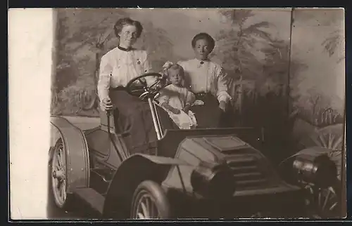Foto-AK Auto Autocar (1903), Zwei junge Frauen mit Kleinkind vor eine Studiokulisse