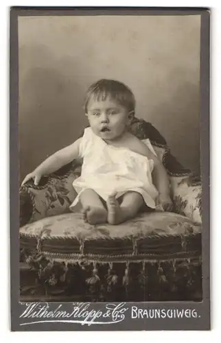 Fotografie Wilhelm Klopp & Co., Braunschweig, Niedliches Baby mit weit aufgerissenem Mund im weissen Kleidchen