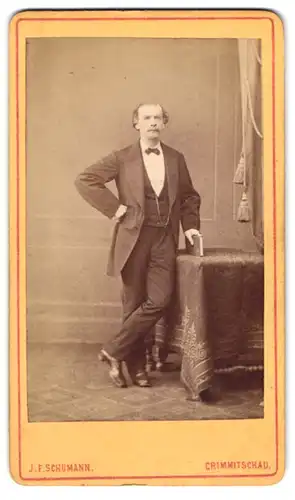 Fotografie J. F. Schumann, Crimmitschau, Adretter junger Herr im schwarzen Anzug mit Fliege und Arm in Hüfte gestemmt