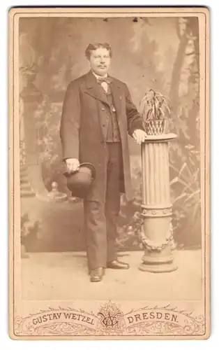Fotografie Gustav Wetzel, Dresden, Prager Strasse 6, Eleganter Herr mit Hut in der Hand, an eine Säule gelehnt