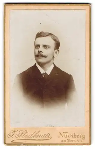 Fotografie J. Stadlmair, Nürnberg, Eleganter junger Herr im schwarzen Anzug mit dunklem Schnurrbart und Seitenscheitel